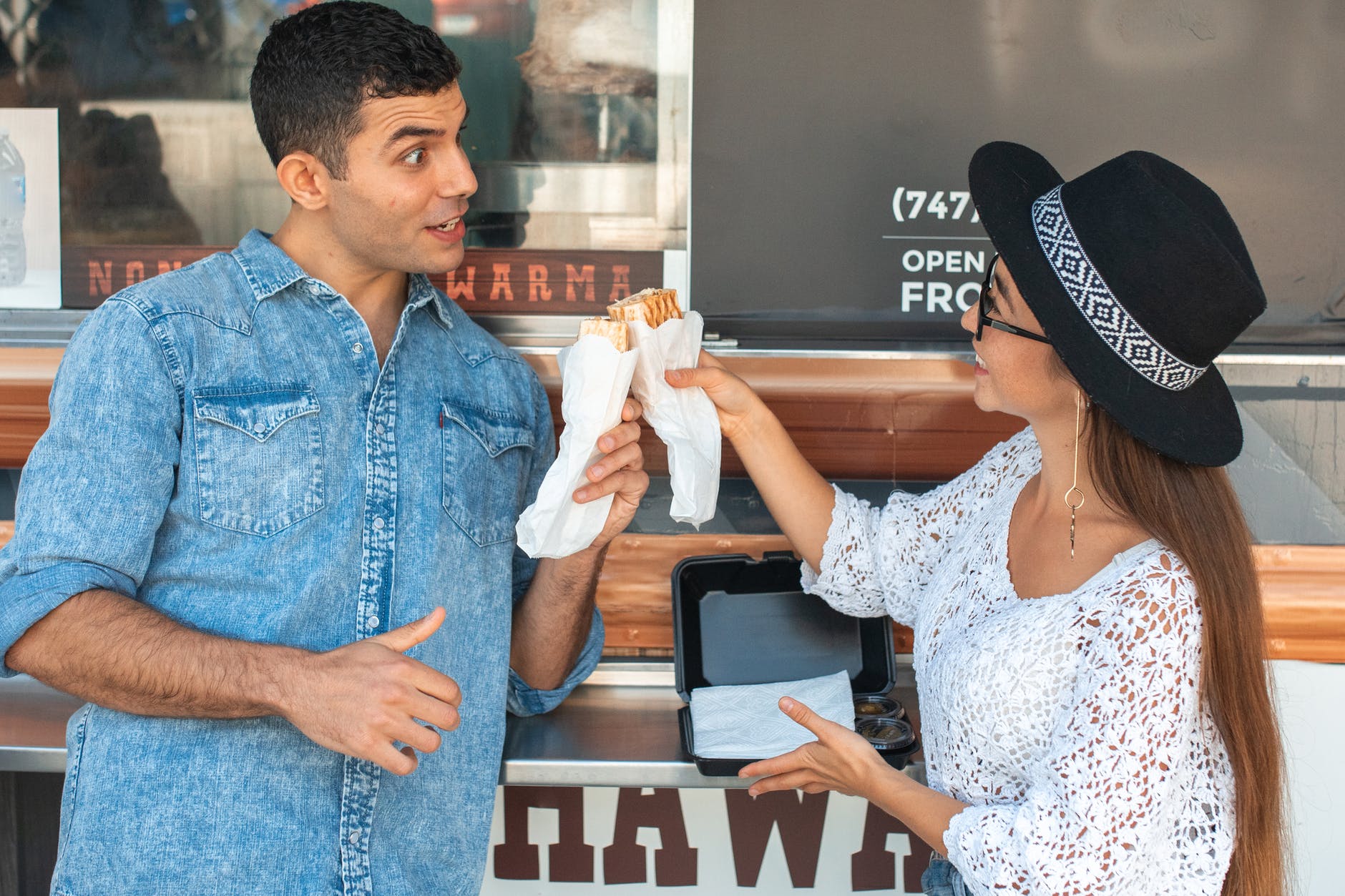 joyful couple clinking sandwiches near food truck